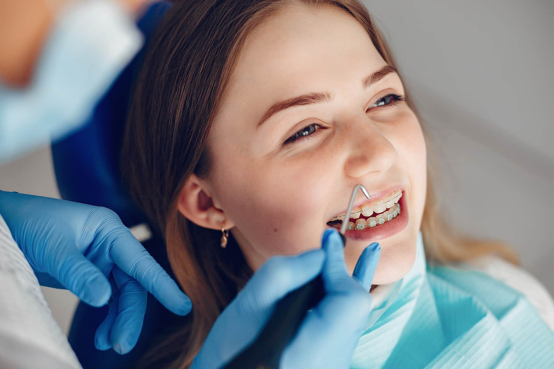 During an appointment at Andros Orthodontics in Pasco, WA, a dentist wearing blue gloves examines a young woman's adult braces with dental instruments.