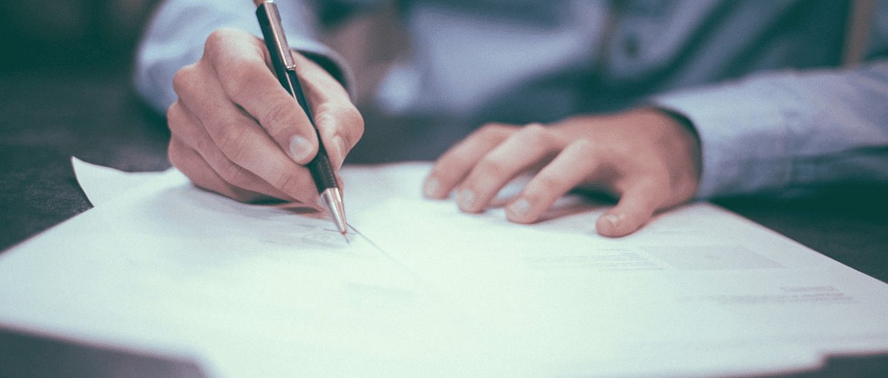 At Andros Orthodontics in Pasco, WA, someone in a blue shirt reviews and writes on papers, possibly related to orthodontic insurance plans, with additional documents spread on the desk.